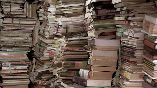 Several piles of books and papers stacked from floor to ceiling